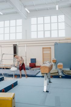 Young male gymnast preparing for practice in a well-equipped indoor gym.