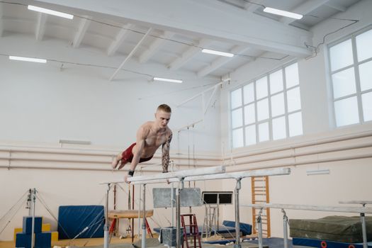 A male gymnast displays strength and skill on the parallel bars in an indoor gym setting.