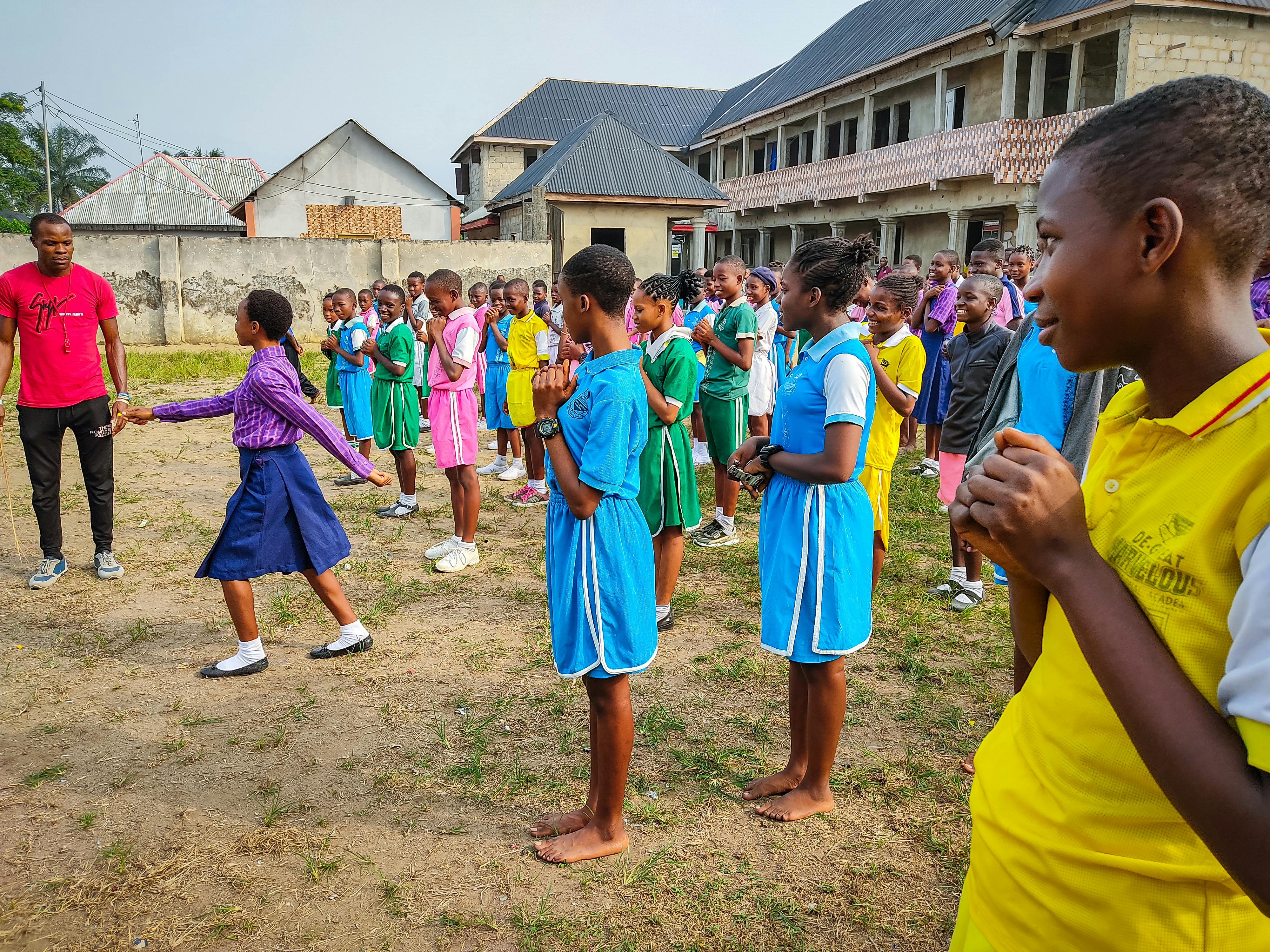 Group of African schoolchildren in uniforms engaging in outdoor activity on school grounds.