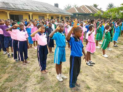 Schoolchildren in colorful uniforms saluting outdoors