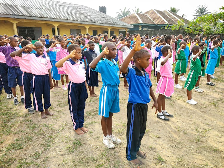 A Large Group Of Children Standing In Rows And Saluting 