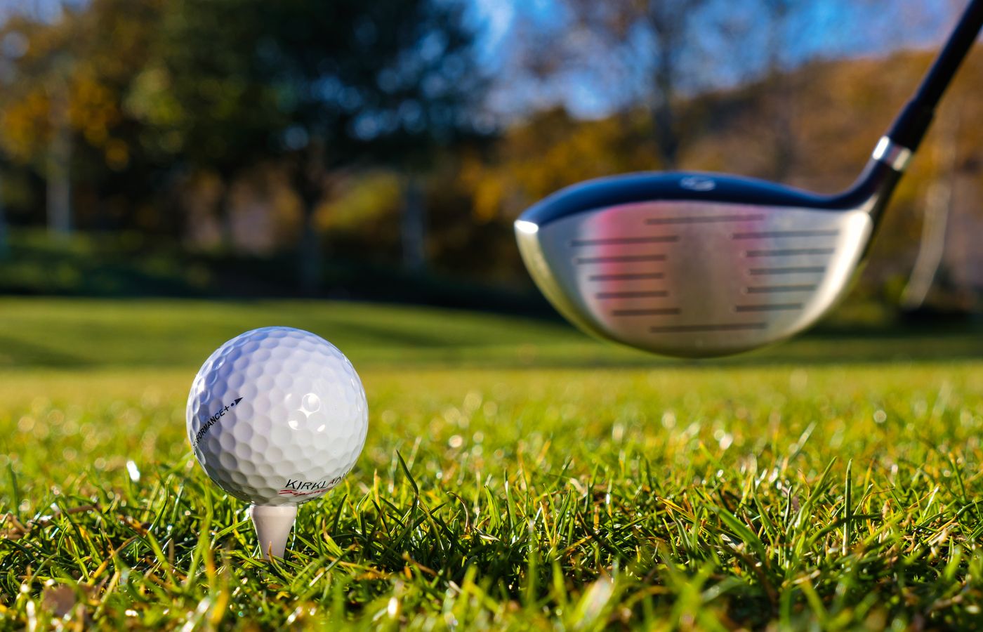 Close-up of a golf ball on a tee with a golf club in sunny weather on a grassy course.
