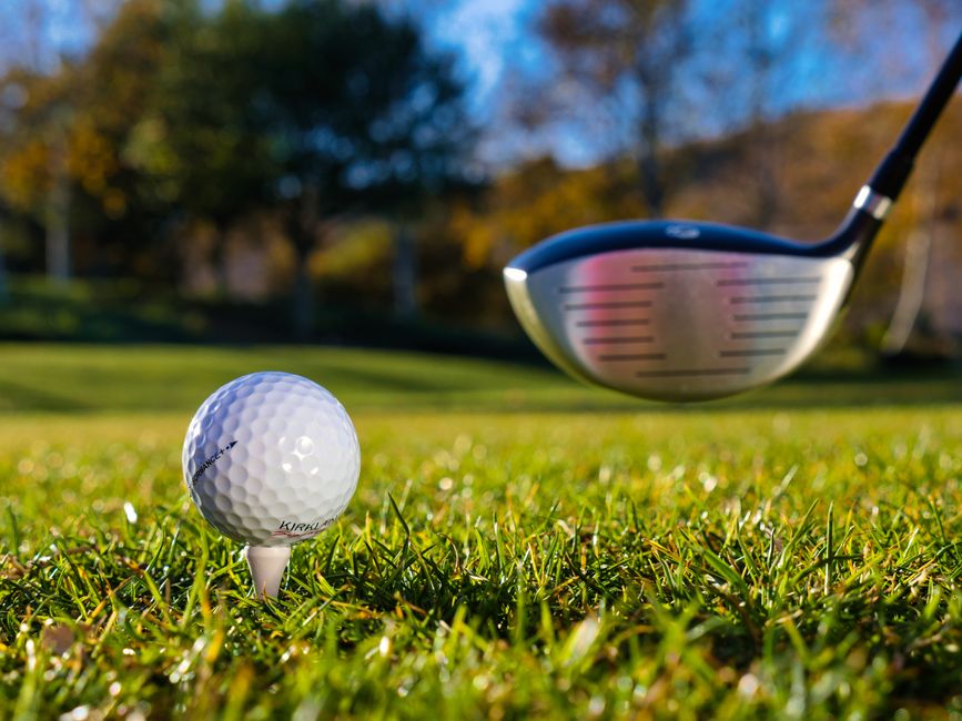Close-up of a golf ball on a tee with a golf club in sunny weather on a grassy course.