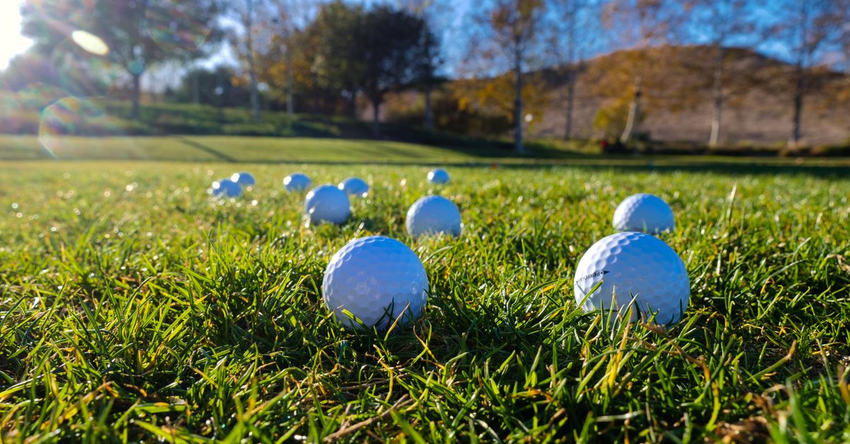 Golf balls scattered on a lush green course under a clear blue sky.