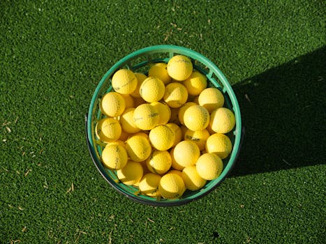 Top view of a basket filled with yellow golf balls placed on bright green artificial turf.