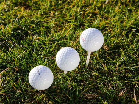 Three golf balls positioned on lush green grass with one on a tee, perfect for sports enthusiasts.