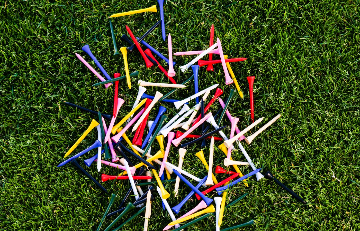 A colorful assortment of golf tees scattered on lush green grass, perfect for sports themes.