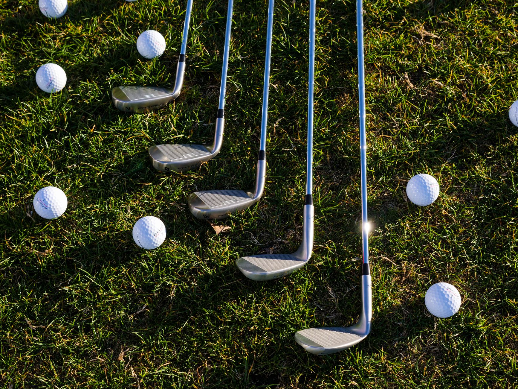 Flat lay of golf clubs and balls arranged on green grass, perfect for sports enthusiasts.