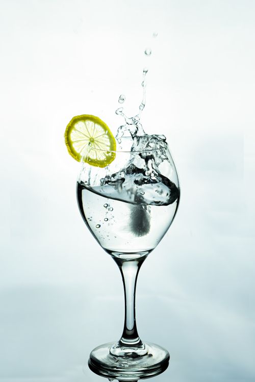 Free A lemon slice splashes into a glass of water, creating dynamic ripples and bubbles. Stock Photo