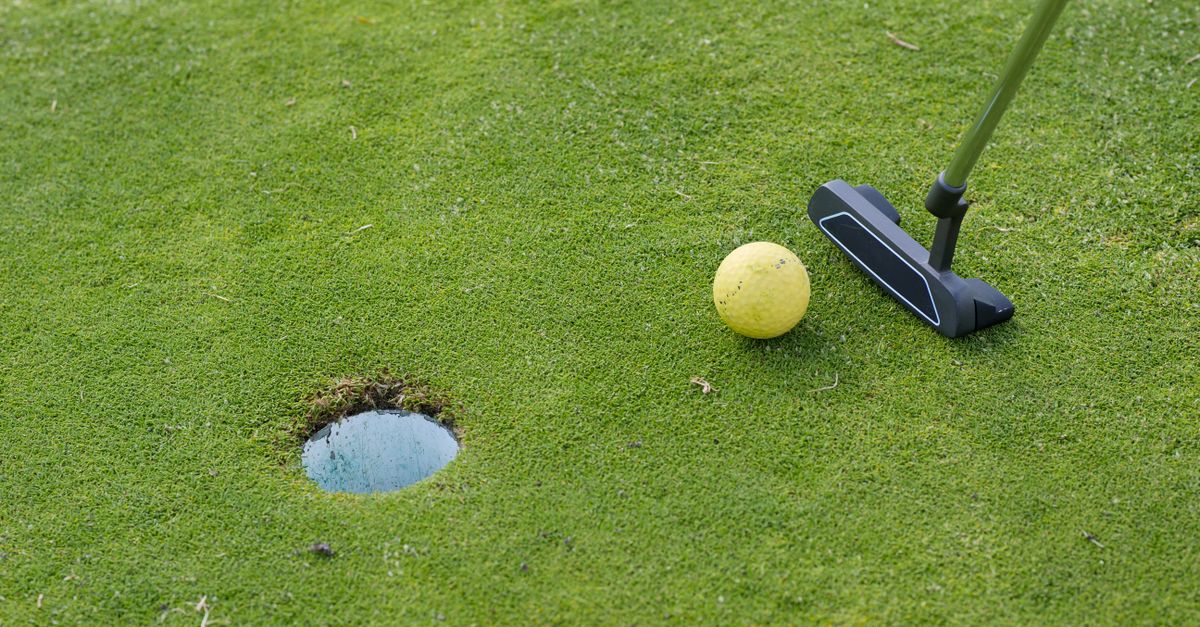 A golf ball and putter near a hole on a lush green golf course, ready for a putt.