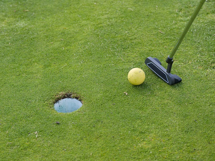 A Golf Putter And Ball Near The Green Hole