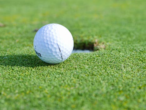A close-up image of a golf ball near a hole on a vibrant green golf course.