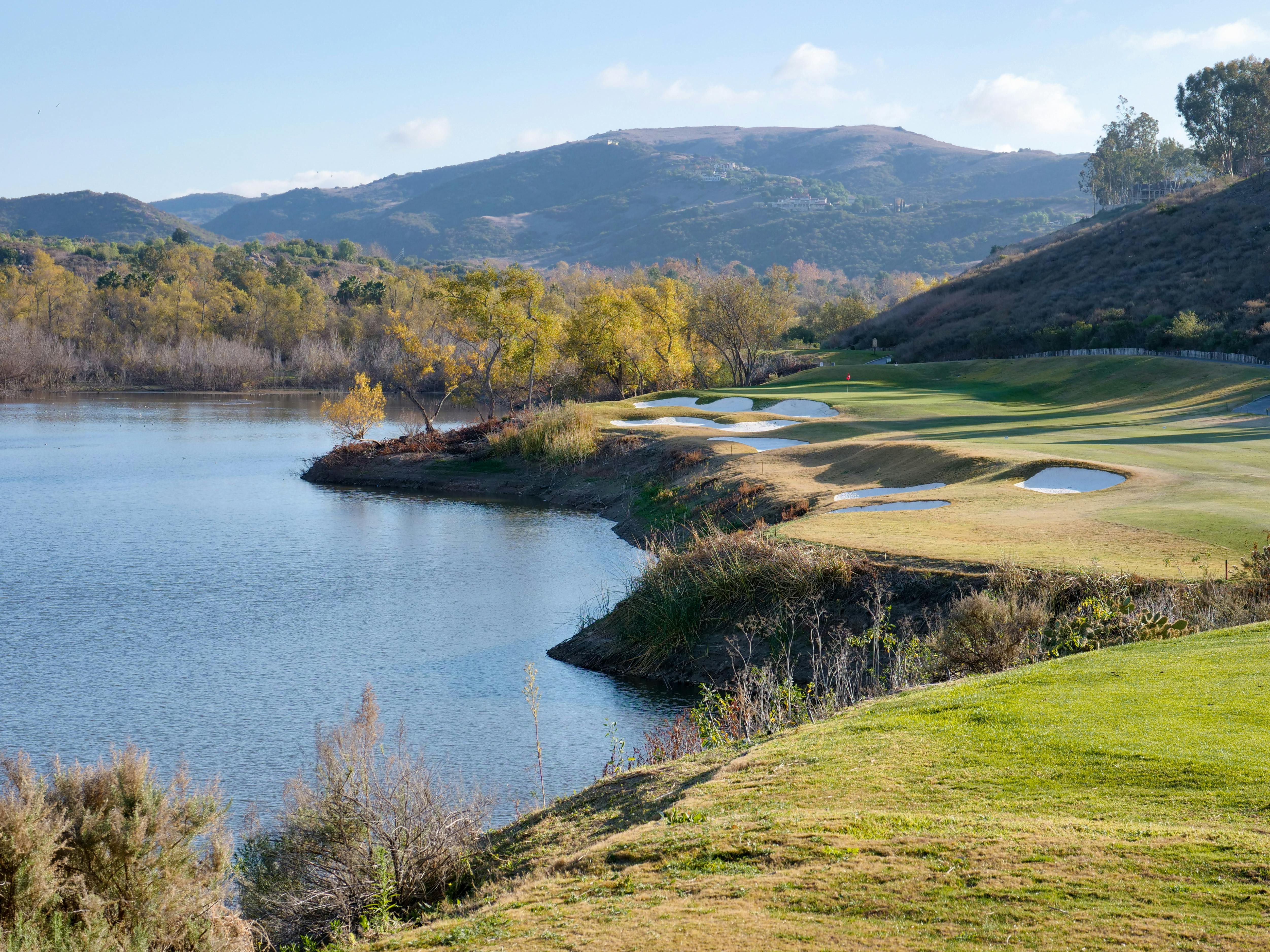 Beautiful landscape view of a golf course by a tranquil lake with distant mountains.