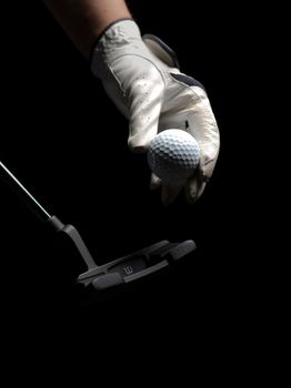 Close-up of a gloved hand holding a golf ball with a club on a dark background.