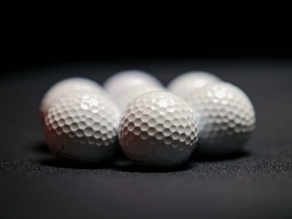 Close-up of plain white golf balls on a dark surface, their dimples catching the light