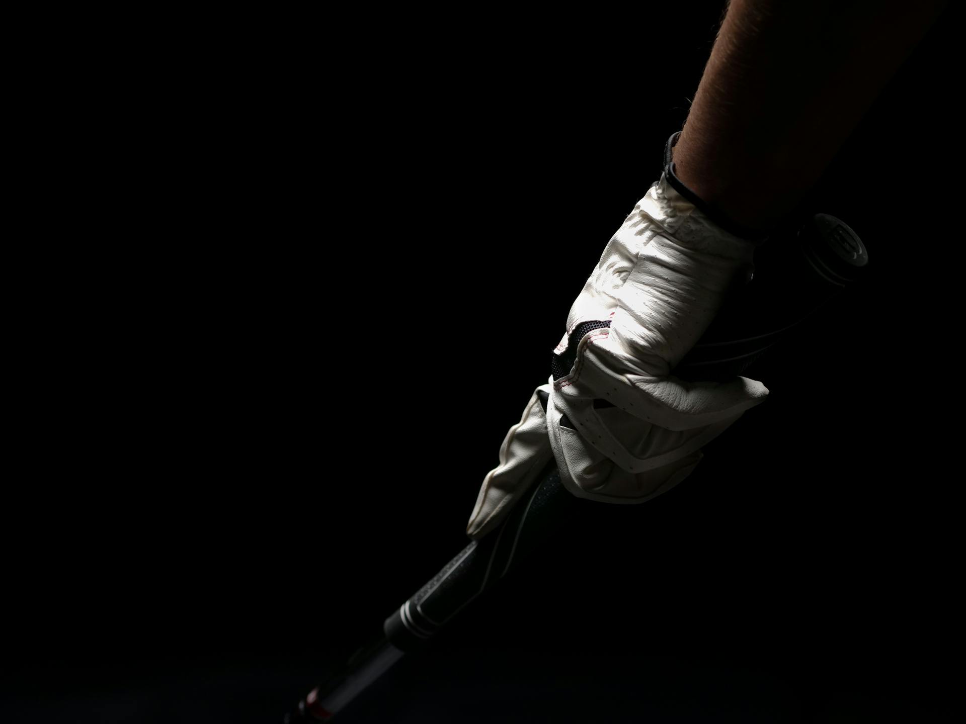 A close-up shot of a golfer's hand in a white glove gripping a golf club against a black background.