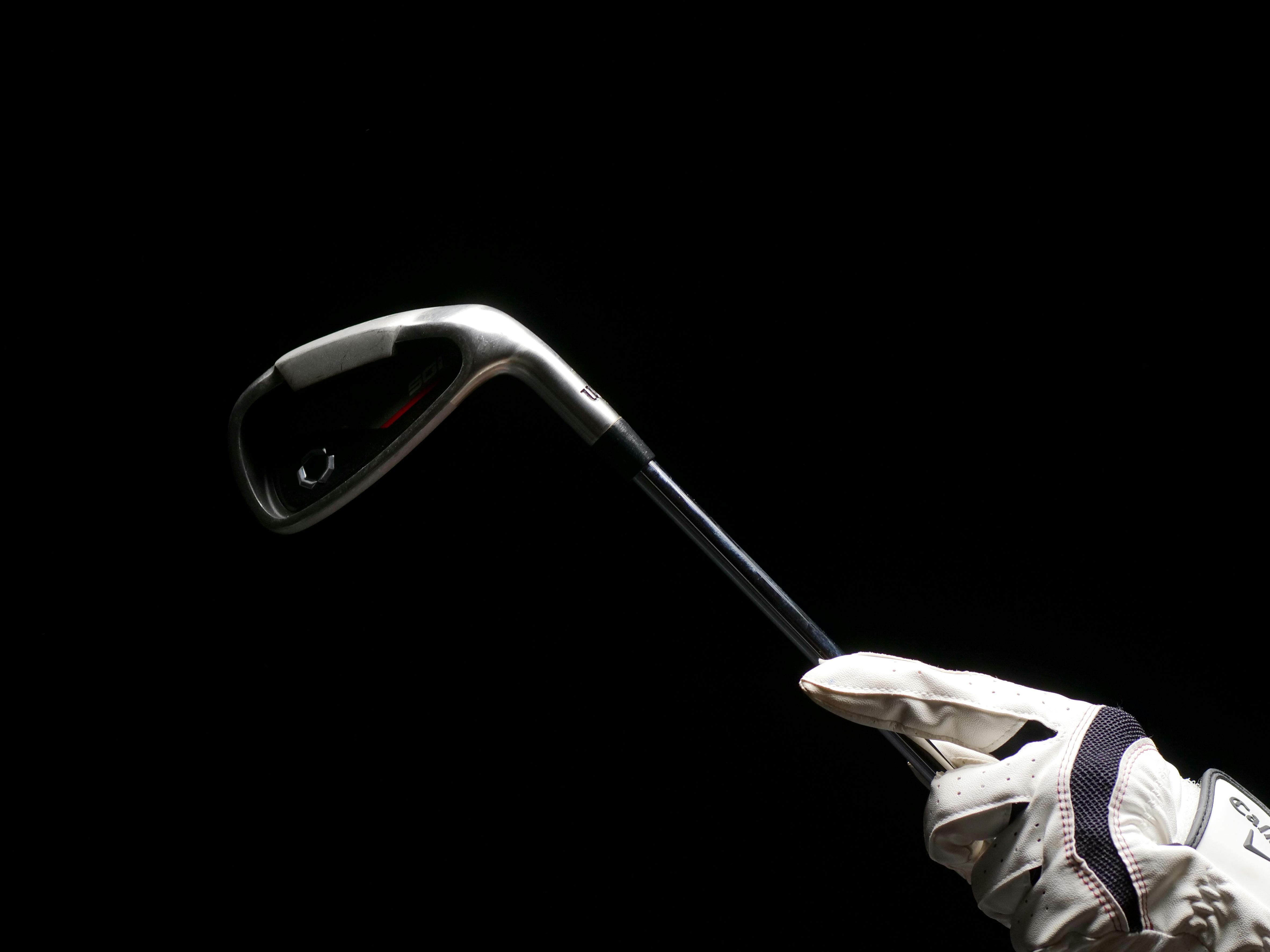 Minimalist image featuring a golf club held by a gloved hand against a black background, highlighting sports equipment.
