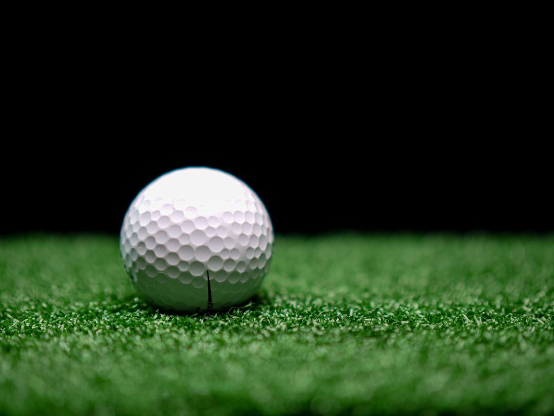 Dimpled golf ball resting on short artificial turf against a dark background