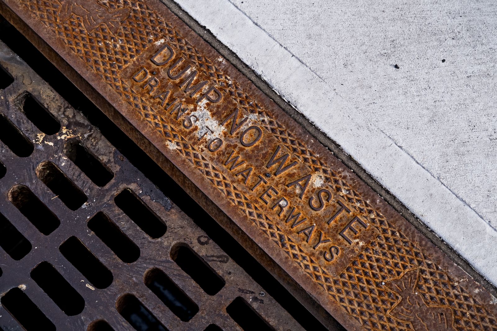 Metal street drainage grate set into a concrete sidewalk