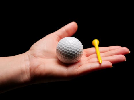 Close-up image of a golf ball and tee in an open palm against a dark background.