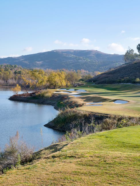 Beautiful green golf course nestled beside a serene mountain lake with clear blue skies.