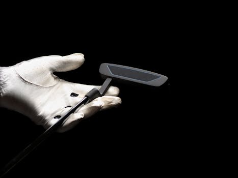 A close-up image focusing on a golf putter held by a gloved hand against a black background.
