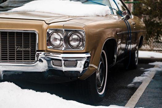 A vintage Oldsmobile car partially covered in snow, showcasing wintertime parking.