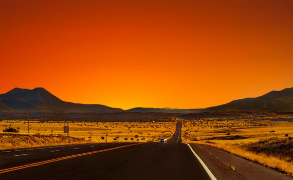 Stunning Arizona highway at sunset with orange sky and desert mountains.