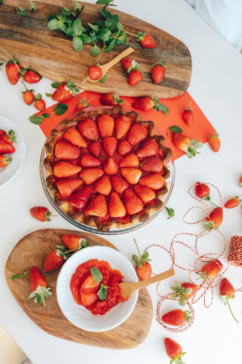 Free Top view of a freshly baked strawberry pie with scattered strawberries on a wooden board. Stock Photo