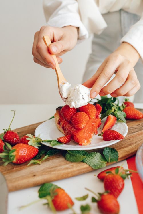 Free A person prepares a delicious strawberry dessert with whipped cream on a ceramic plate. Stock Photo