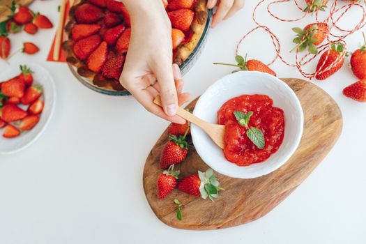 Close-up of hands making fresh strawberry jam with mint garnish.