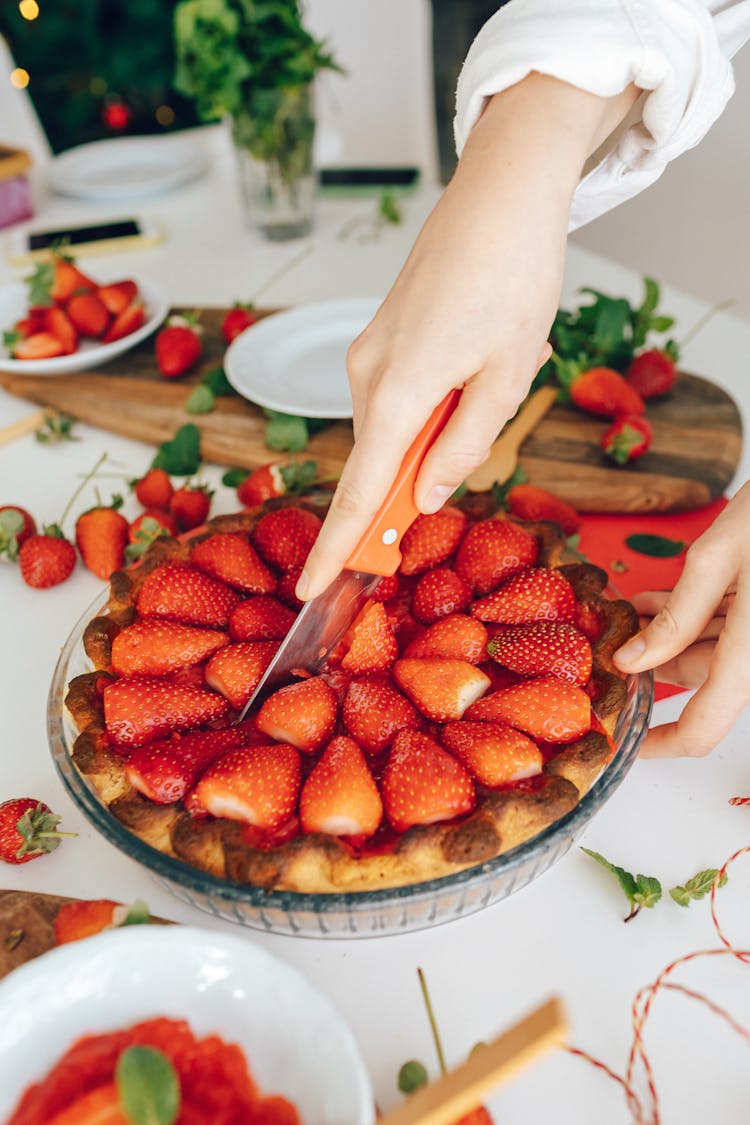 Person Slicing A Strawberry Pie On Glass Bowl