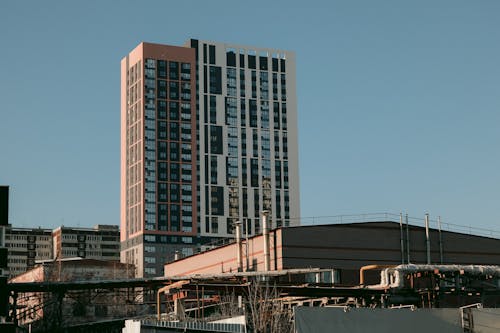 Low angle exterior of contemporary high rise residential building in urban district against cloudless blue sky