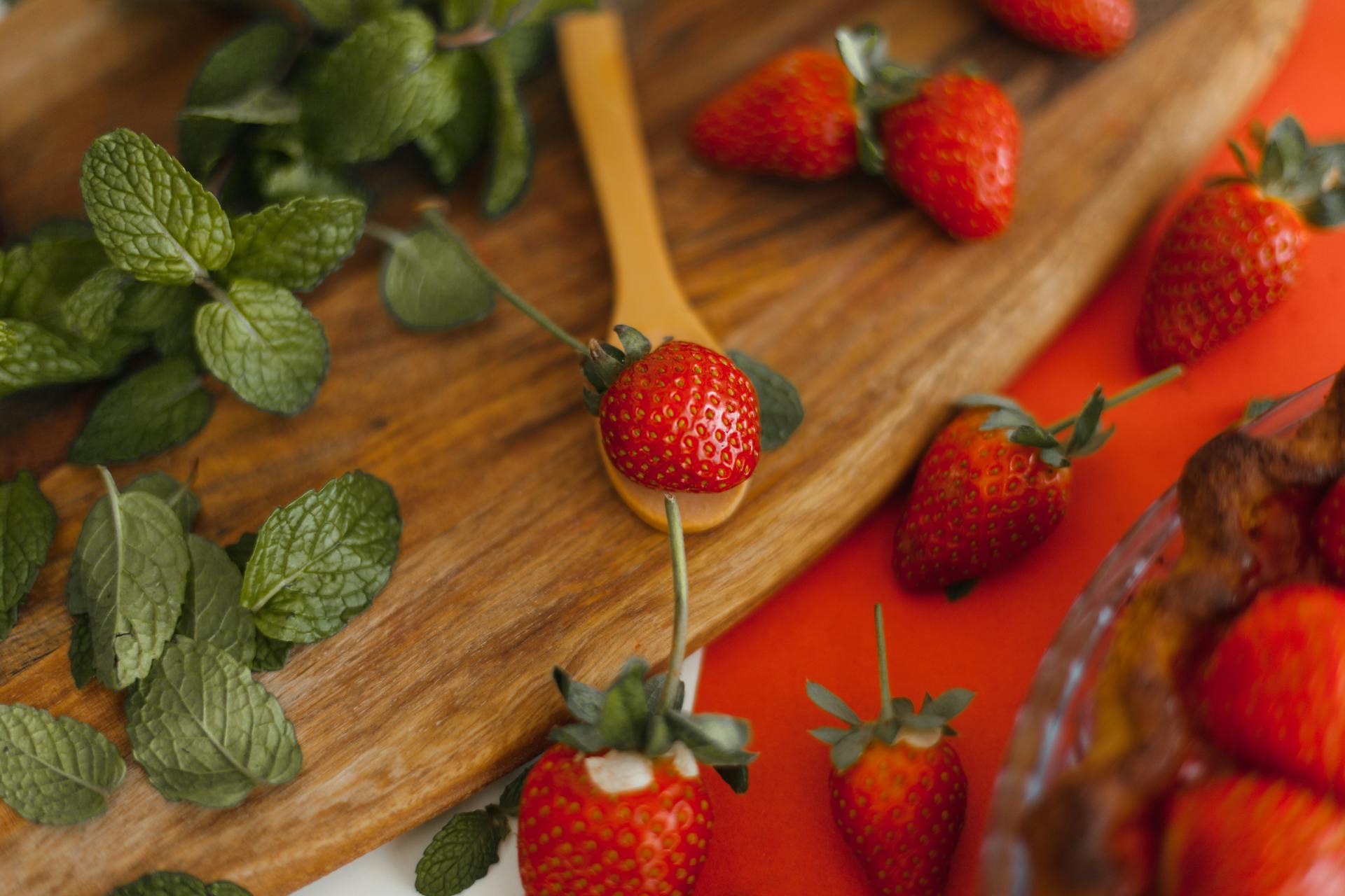 Fresh strawberries and mint leaves arranged on a wooden board, perfect for food inspirations.