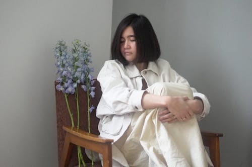 Asian woman in stylish outfit resting in armchair with flowers