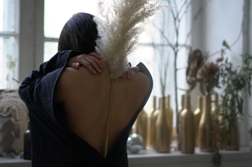 Free Back view of anonymous woman with naked back holding dried plant while standing in room with decorative plants and vases in daylight Stock Photo