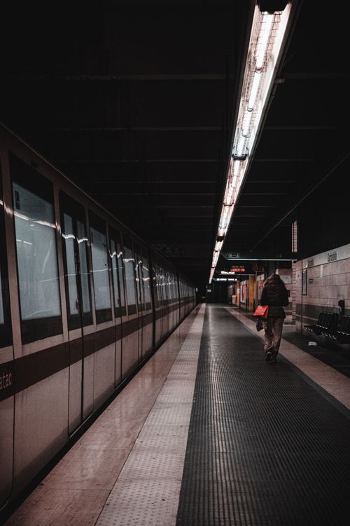 Free A lone person walks on a dimly lit urban train station platform at night. Stock Photo