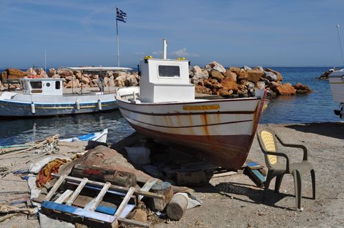 Free Fishing boats docked at a scenic harbor on Chios Island, Greece, under a clear blue sky with a Greek flag waving. Stock Photo