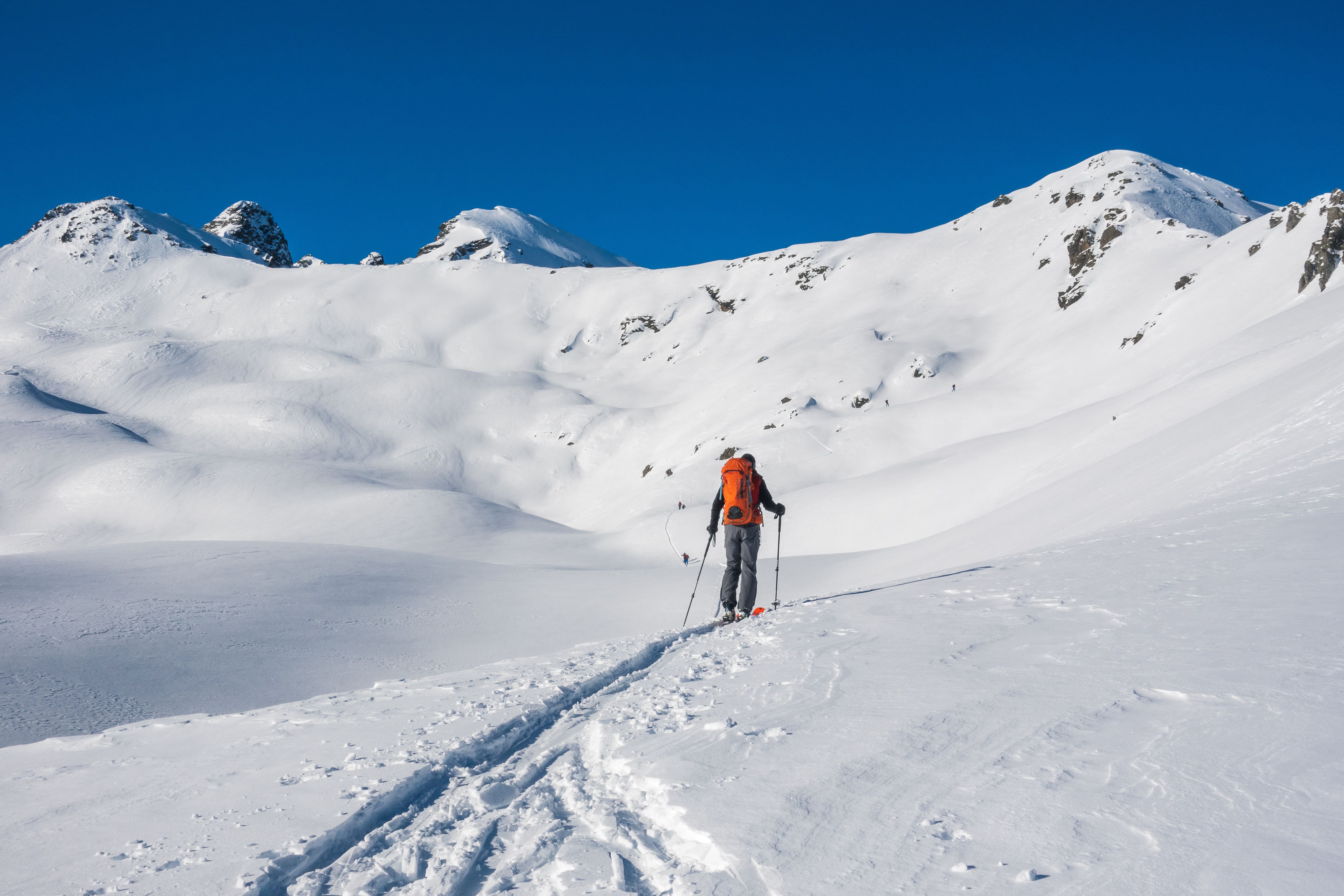 Lone ski tourer with backpack traversing snowy mountains under a clear blue sky