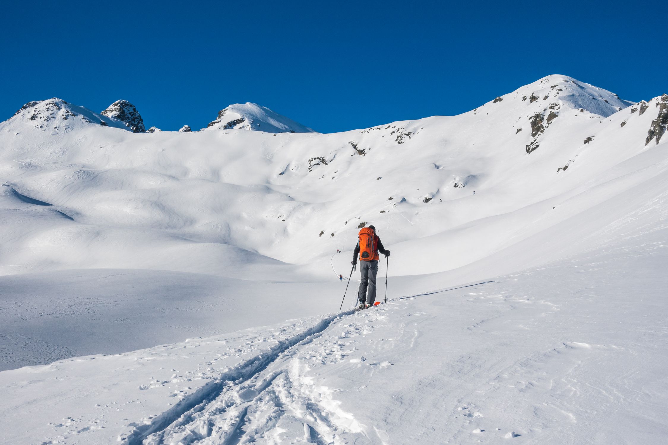Lone ski tourer with backpack traversing snowy mountains under a clear blue sky
