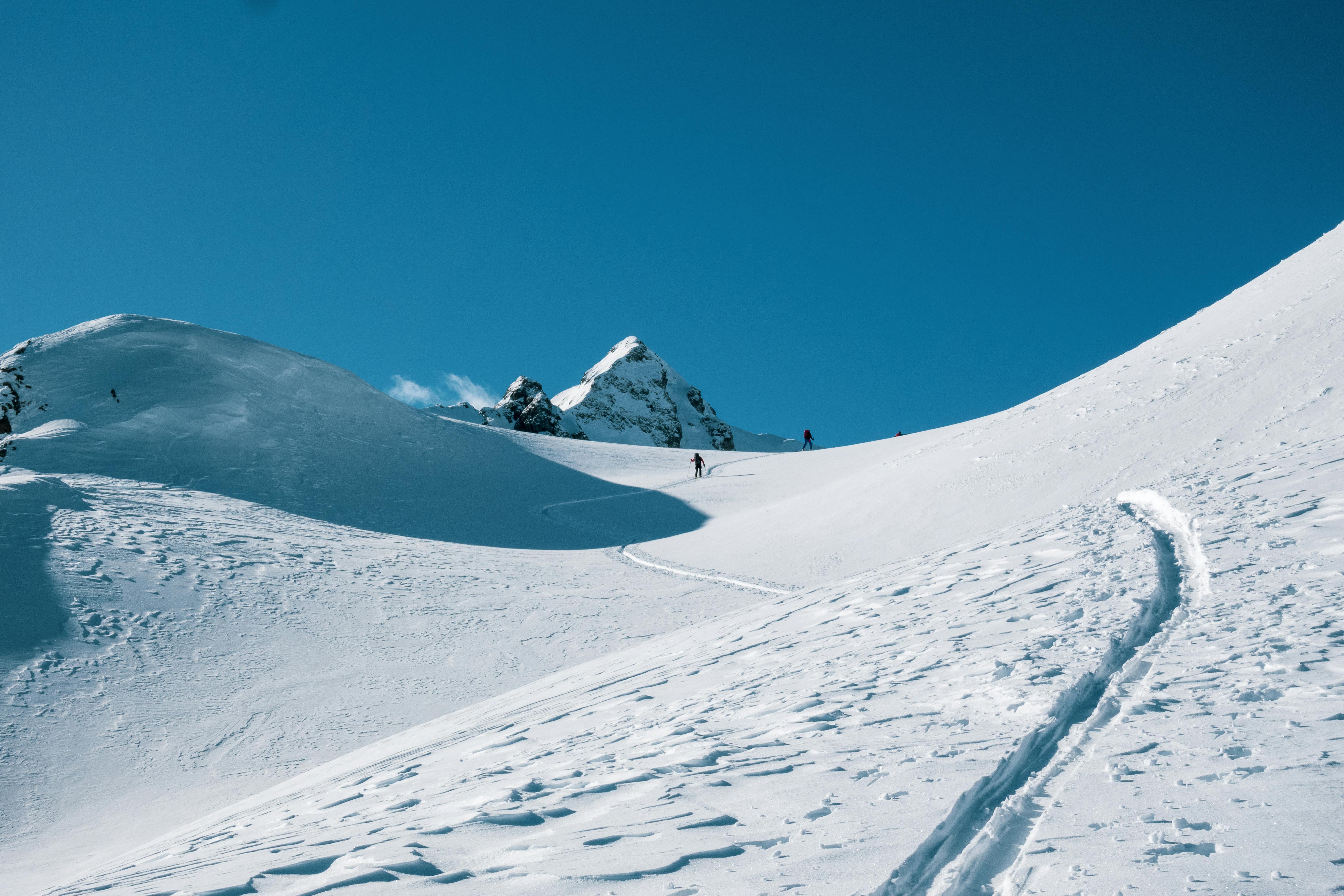 Skiers traverse a snowy mountain under a bright blue winter sky.
