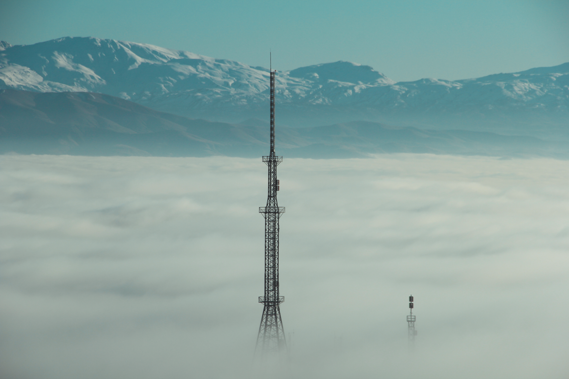 A steel antenna tower rises above a sea of clouds with distant mountains in Turkey. Captivating landscape view.