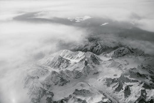 Stunning aerial view of a snow-covered mountain range enveloped in clouds, capturing the essence of winter.