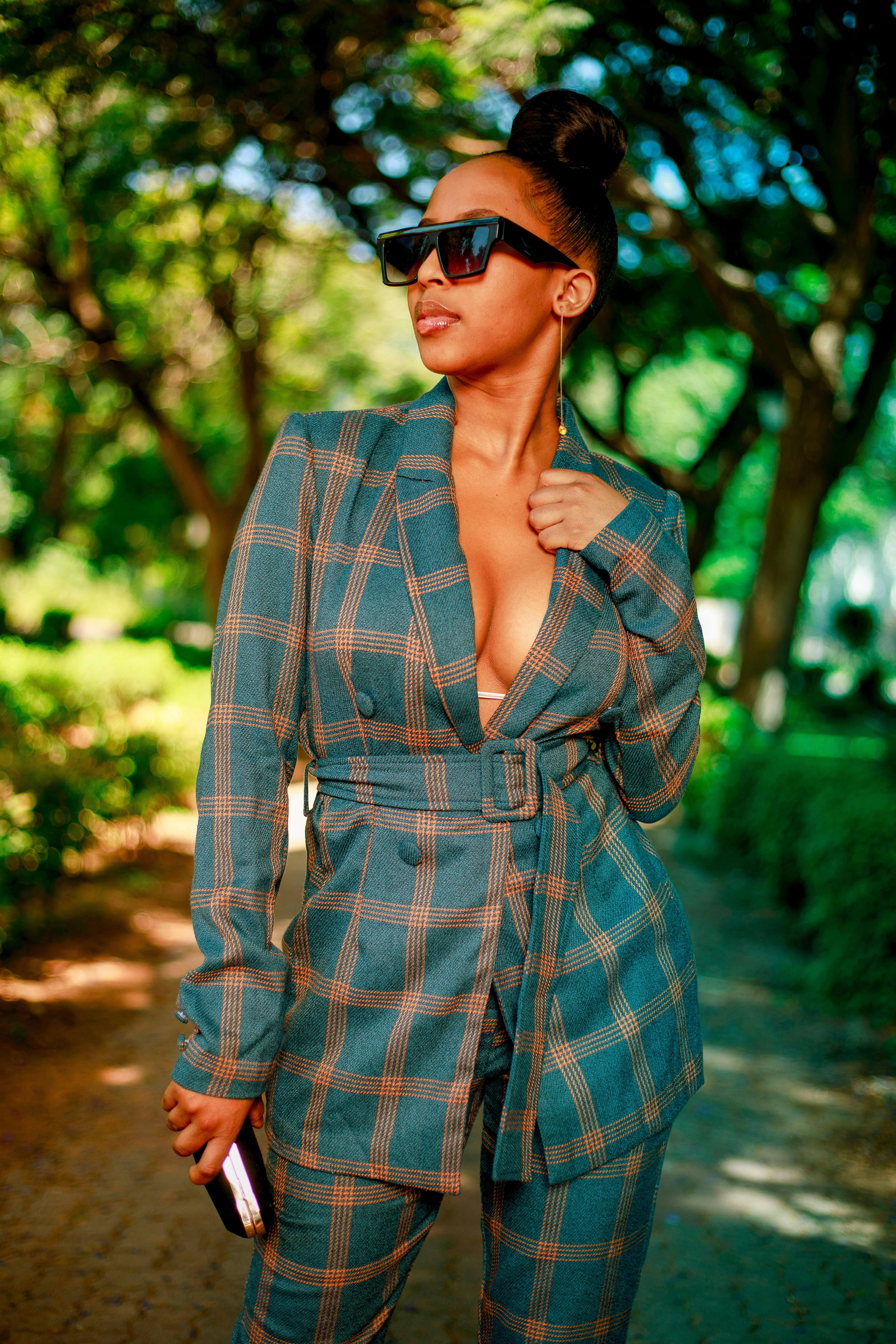 Chic woman in plaid suit posing outdoors under trees, showcasing elegant lifestyle.