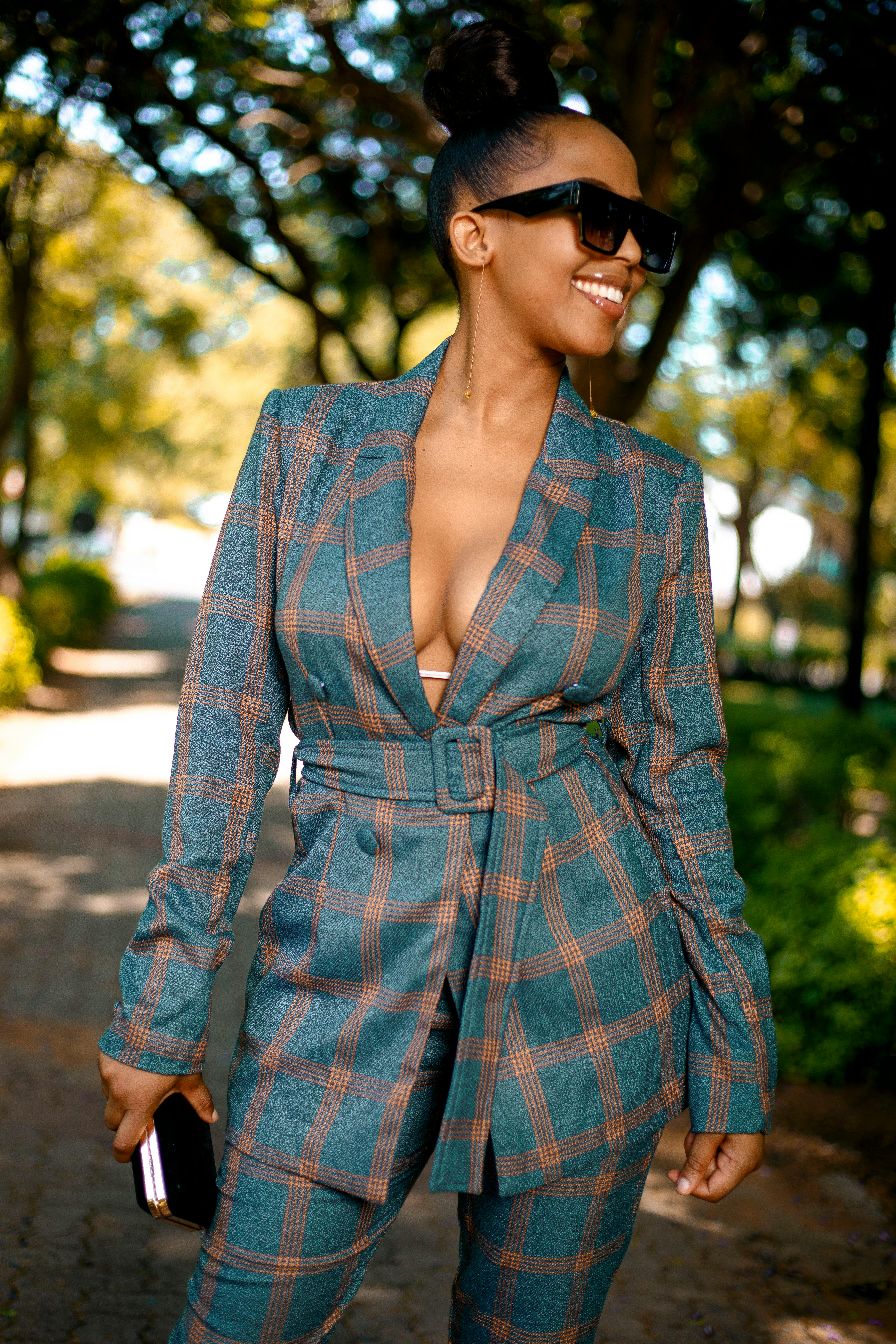 Confident woman wearing a plaid suit and sunglasses smiling outdoors.