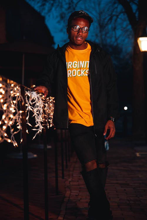 Man Standing Beside Metal Railing with Illuminated Lights