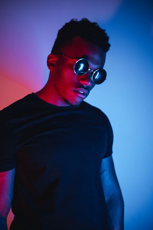 Free Portrait of a man wearing sunglasses under dramatic red and blue lighting, in a studio setting. Stock Photo