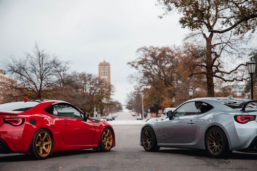 Free Two luxury sports cars parked on an urban street with trees and buildings in the background. Stock Photo