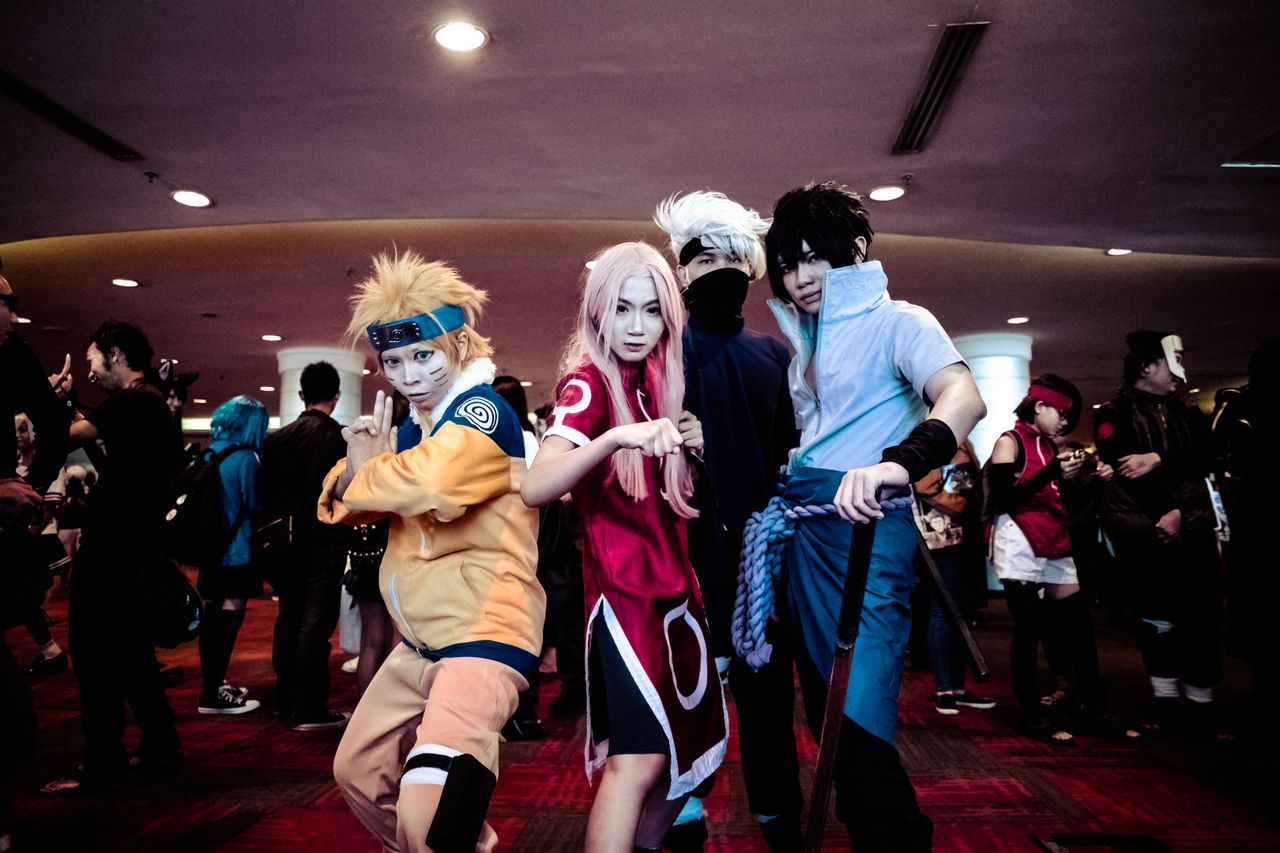 a lively group of cosplayers in anime costumes posing at an indoor con