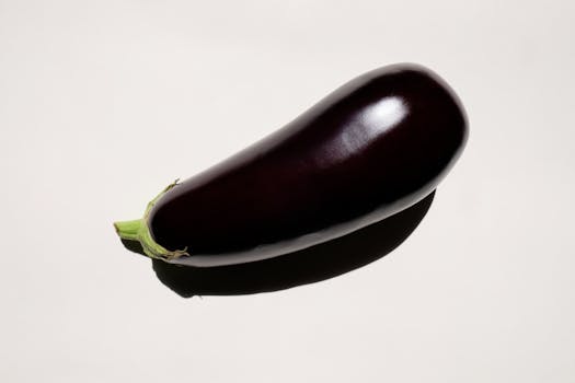 Vibrant close-up of a shiny eggplant with shadow on a light background.
